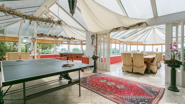A spacious indoor area with a ping pong table, wicker furniture, and a red patterned rug.