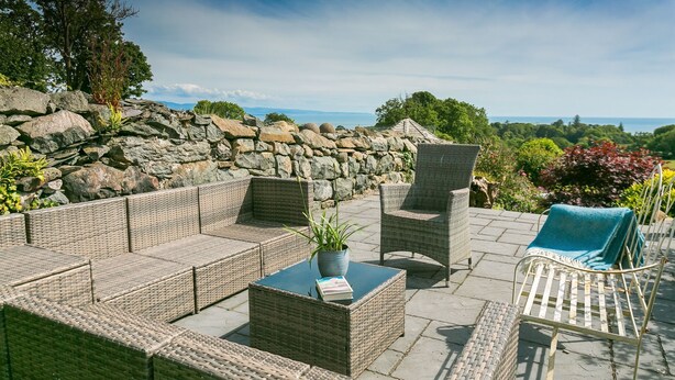 Eine Terrasse im Freien mit Korbmöbeln, einer Steinmauer und Meerblick.