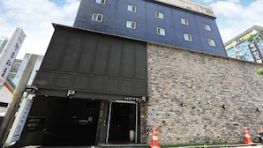 Hotel com fachada moderna, parte inferior em tijolo e placa indicando área de estacionamento.