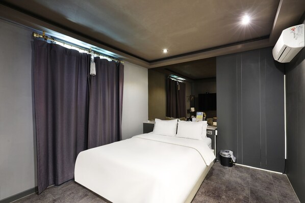 A modern hotel room with a large bed, dark curtains, a small bedside table, a mirror, and an air conditioning unit.