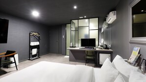 Quarto de hotel moderno com cama, escrivaninha, cadeira e uma grande janela.