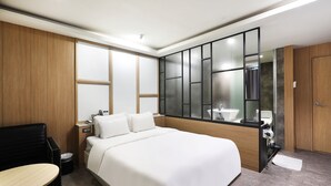 Quarto de hotel moderno com uma cama grande, um guarda-roupa de madeira, uma pequena escrivaninha e um espaço de estar.