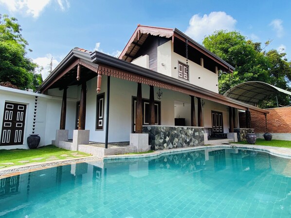 Une maison à deux étages avec une piscine, dotée d’un patio couvert et d’une grande fenêtre.