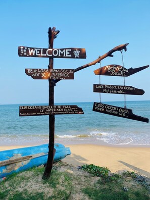 Un panneau indicateur en bois, doté de plusieurs flèches indiquant différentes directions, est installé sur une plage et contient des messages sur la protection des océans.