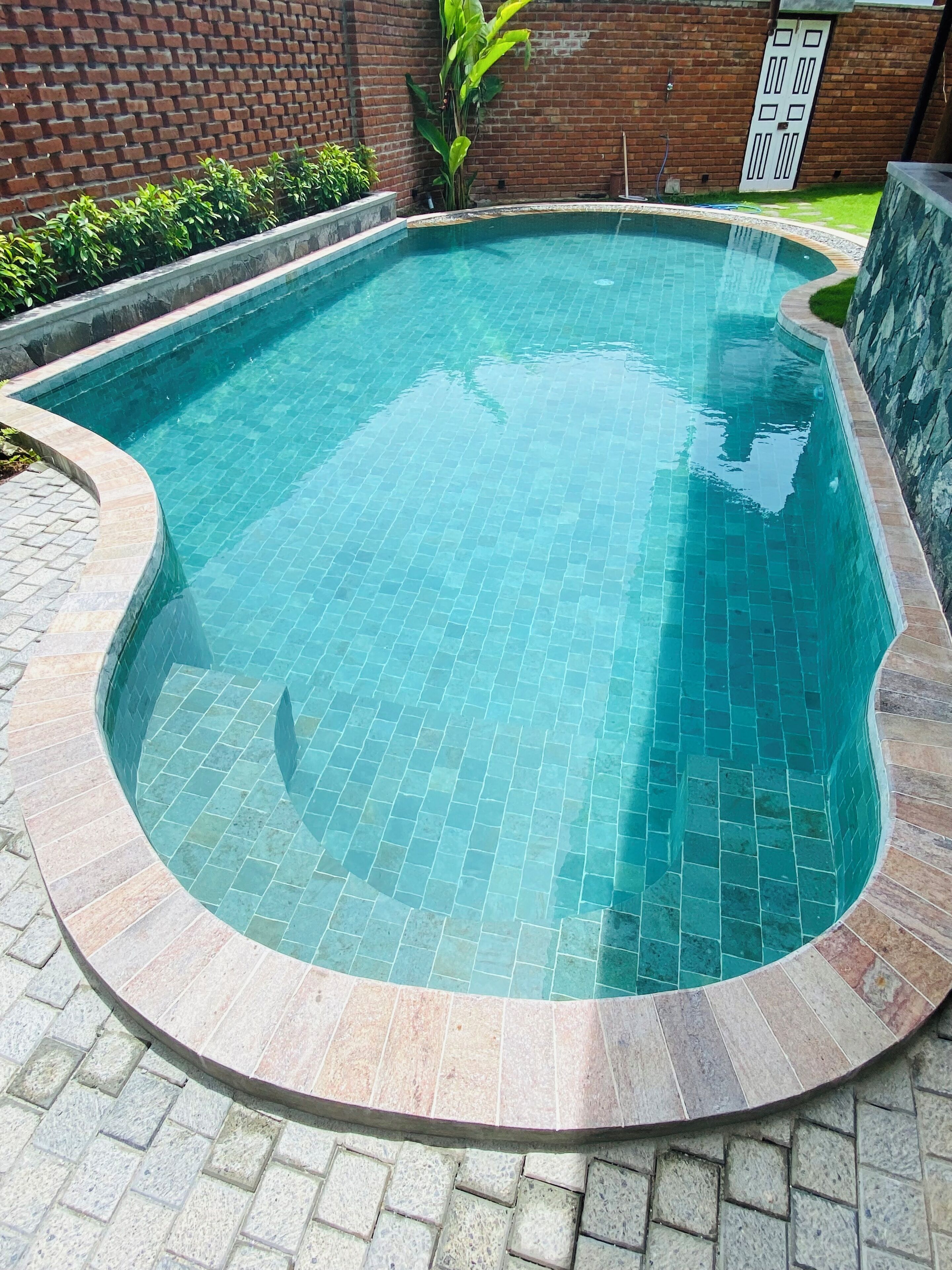 Una piscina con borde de azulejos, rodeada por un muro de ladrillo y un borde de piedra.