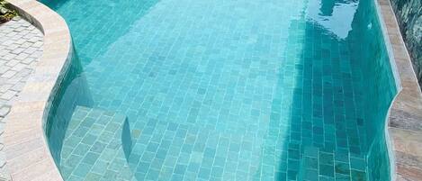 Una piscina con borde de azulejos, rodeada por un muro de ladrillo y un borde de piedra.