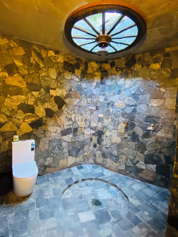 Une salle de bain aux murs en pierre, dotée d’un lavabo rond et de toilettes.