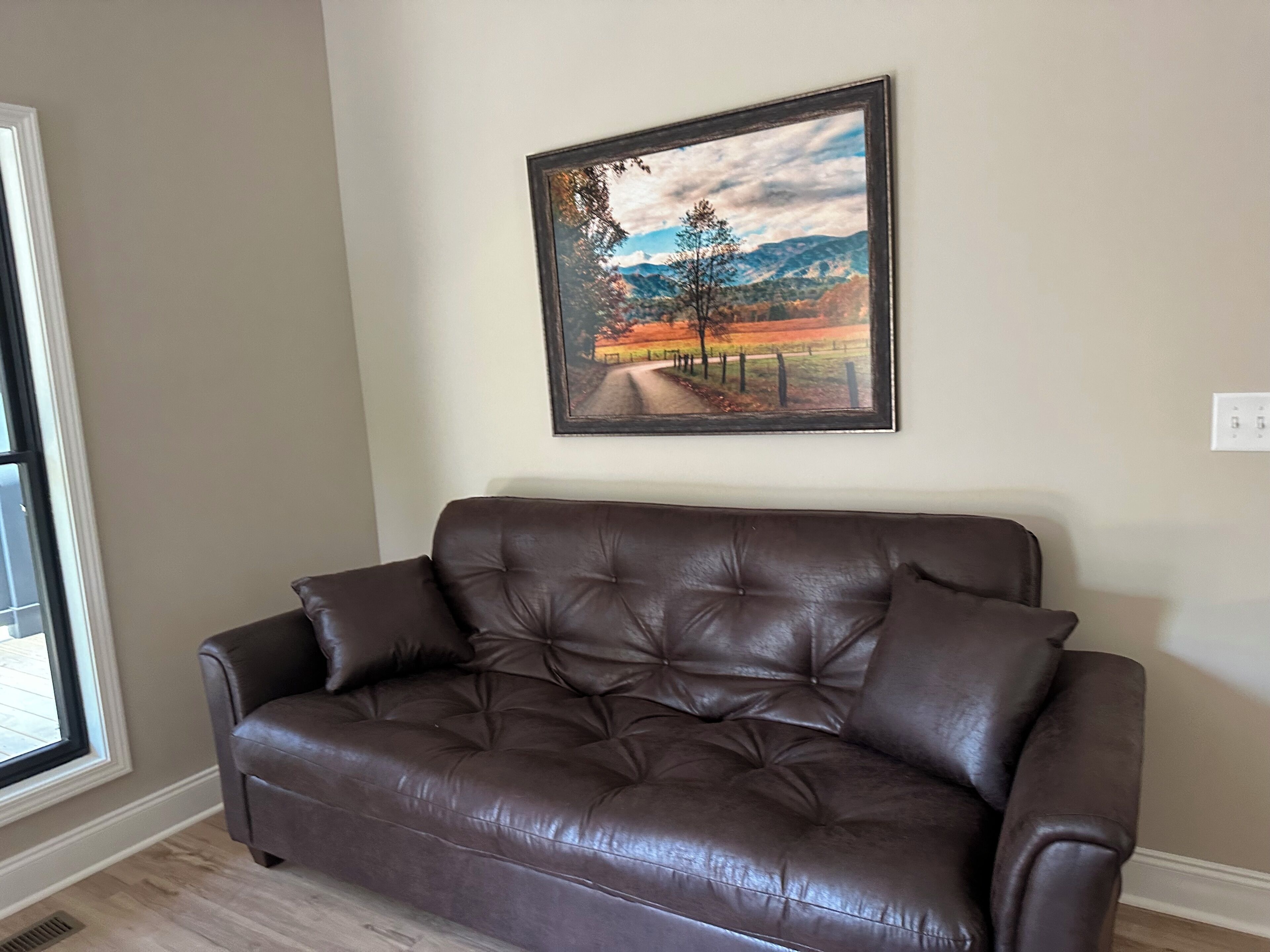 A brown leather sofa in a room with a painting of a landscape on the wall.