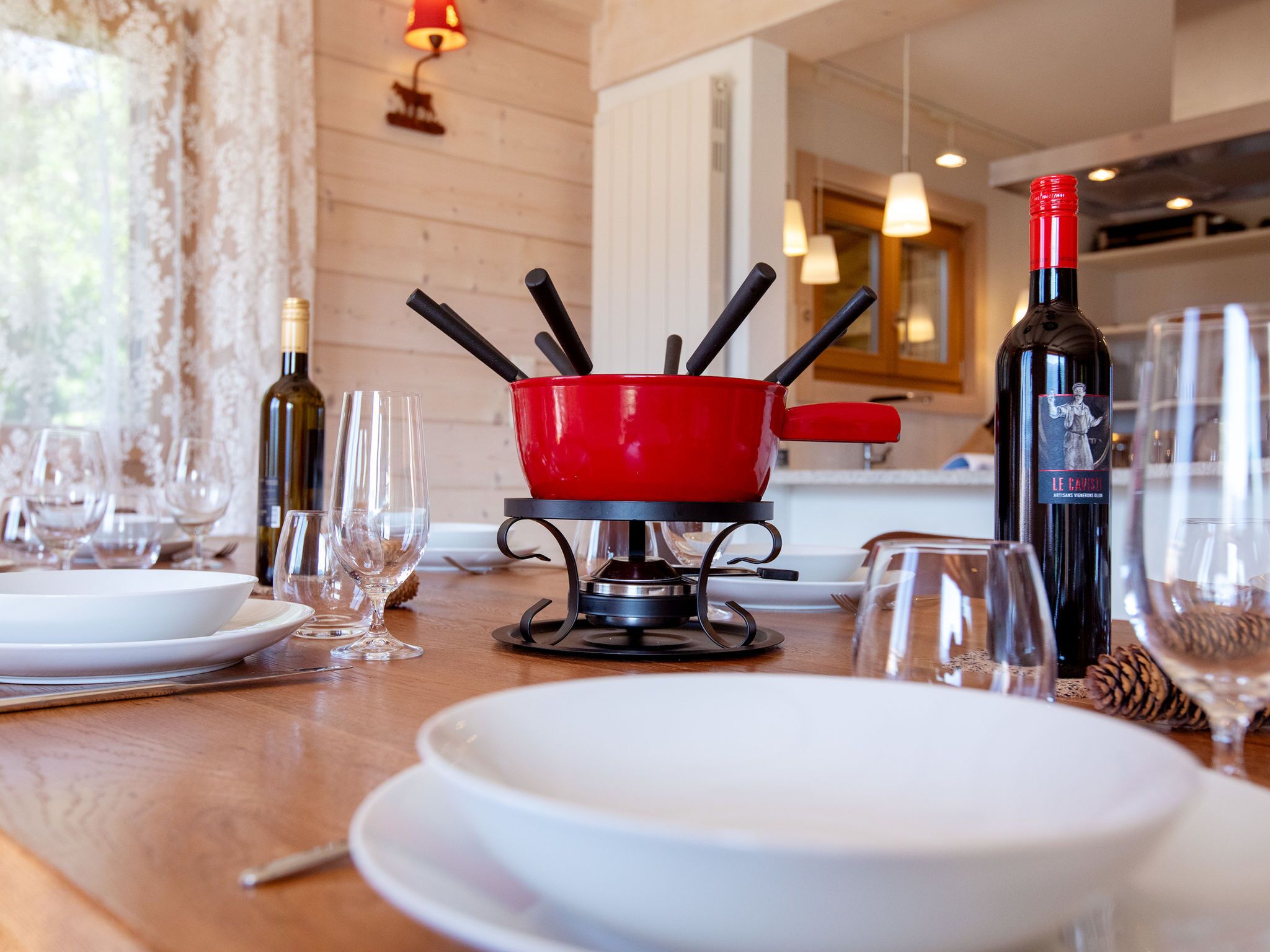 A dining table with a red fondue pot, wine glasses, and bottles.