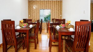 A dining area with wooden tables and chairs, a brick-patterned wall, and a window with bars. - An Vien Hotel (Da Nang)