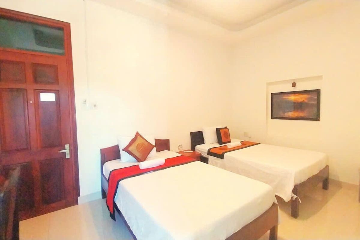 A room with two beds, a wooden door, a framed picture on the wall, and a small table.