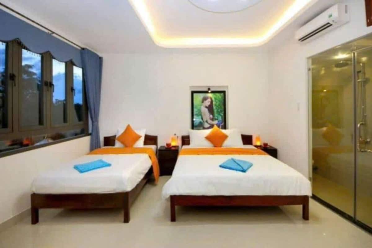 A hotel room with two beds, a large window, an air conditioning unit, and a door.