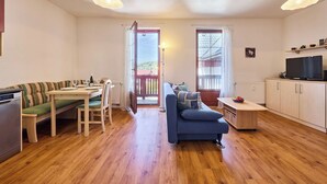 Ein modernes Wohnzimmer mit Holzboden, einer Essecke mit Tisch und Stühlen, einer Couch, einem Fernseher und Blick durch eine Glastür.