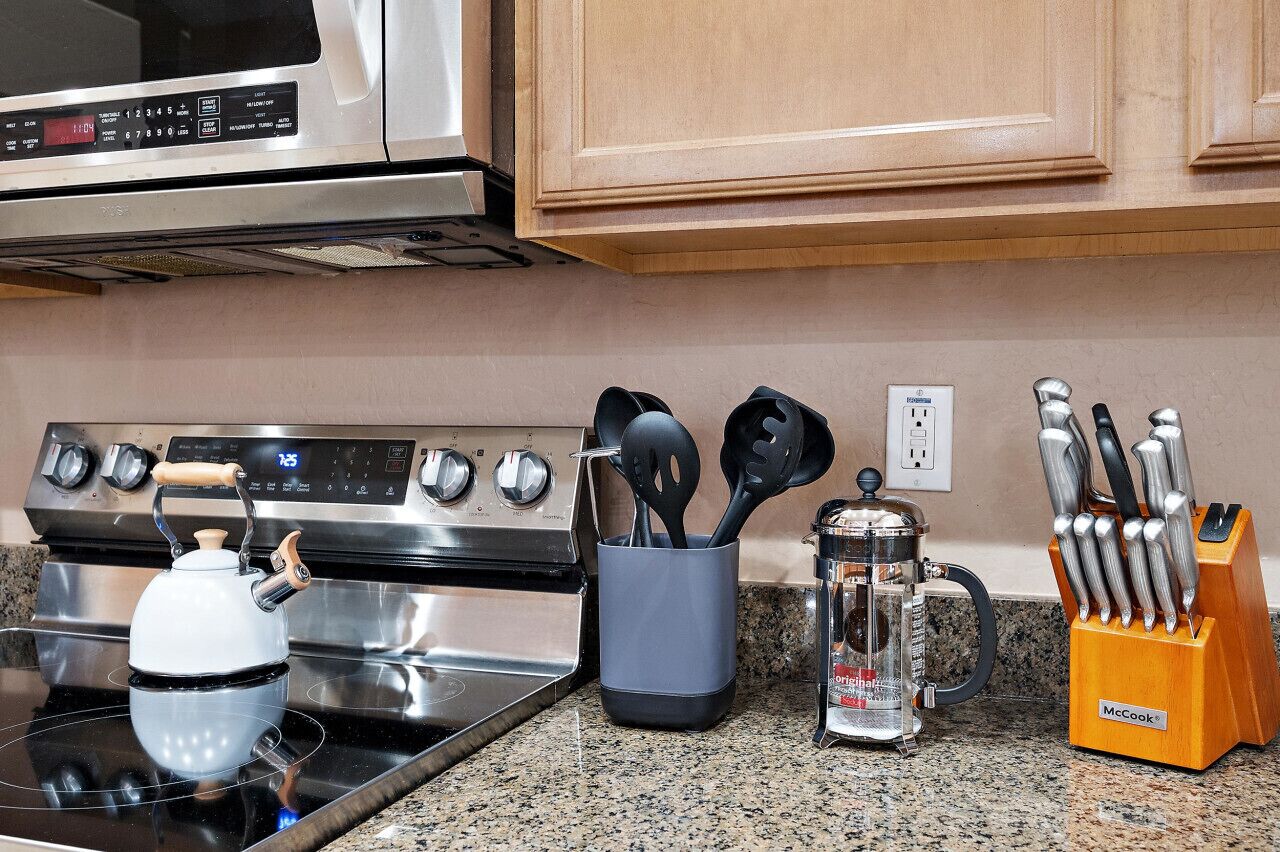 Een keuken met een gasfornuis, een waterkoker, een koffiezetapparaat en een messenblok.