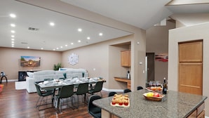 A modern kitchen with granite countertops, a dining area with a white table and chairs, and a living area with a sofa and fireplace.