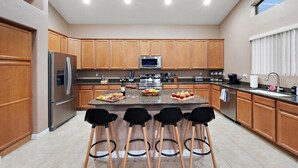 A modern kitchen with wooden cabinets, stainless steel appliances, a central island with bar stools, and a large window providing natural light.
