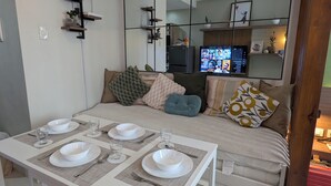 A modern living room with a dining area, a sofa with cushions, a television, and a red toolbox.