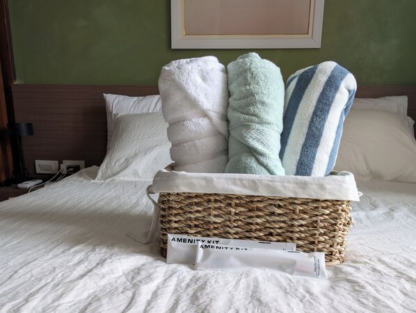 A neatly made bed with a basket containing towels and an amenity kit.