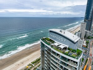 A high-rise hotel with a rooftop terrace overlooking a beach and ocean. - Stunning High Level Deluxe Apartment at Rhapsody (Surfers Paradise)