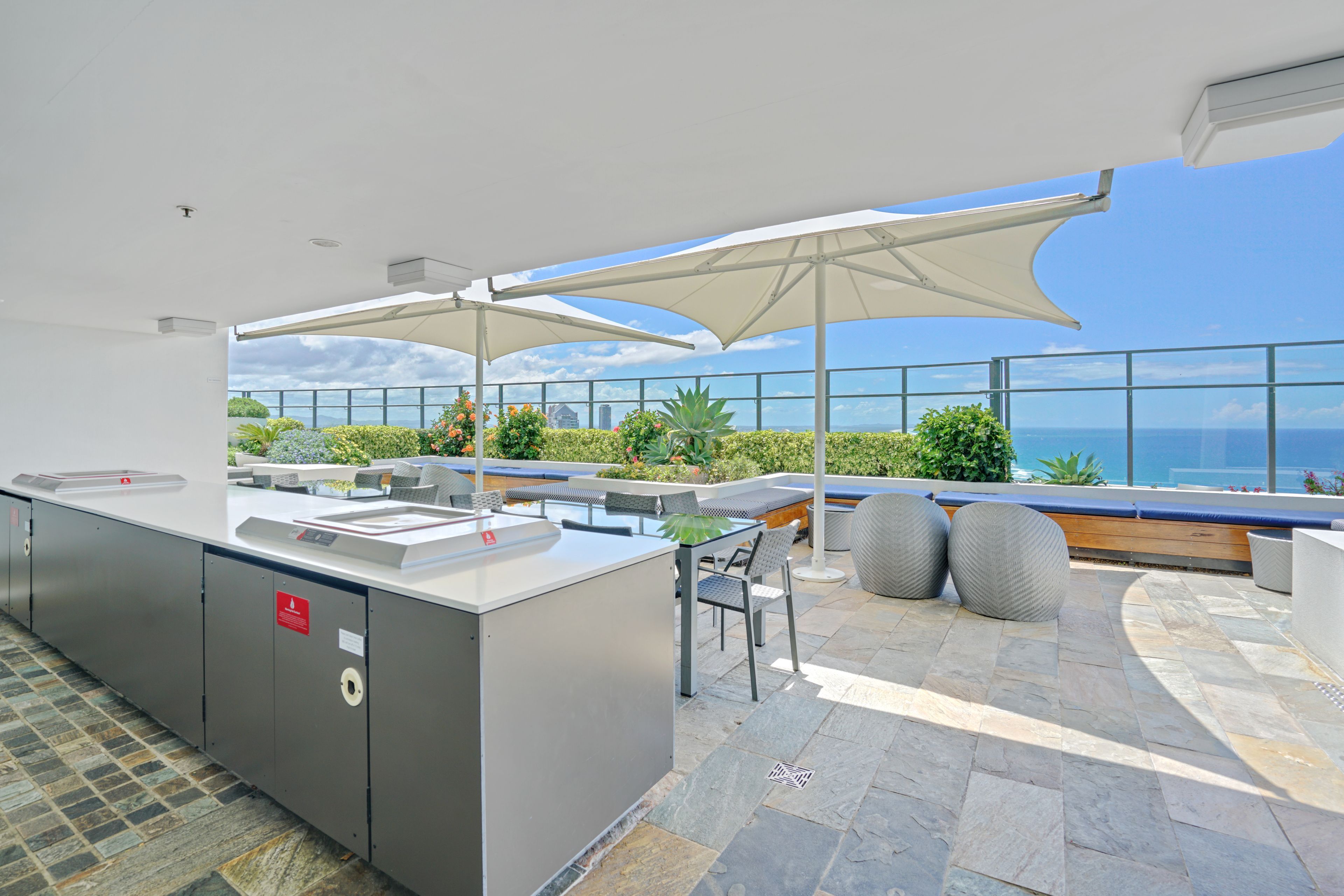 Ein moderner Außenbereich mit Küchenzeile, einer Bar, Sitzgelegenheiten und Blick auf den Ozean.