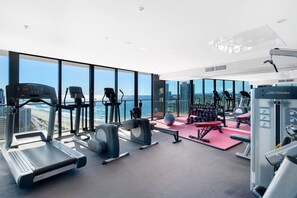 Ett gym med konditionsmaskiner, styrketräningsmaskiner och utsikt över staden.