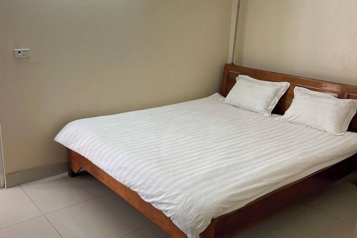 A bedroom with a wooden bed, white bedding, and a light switch on the wall.