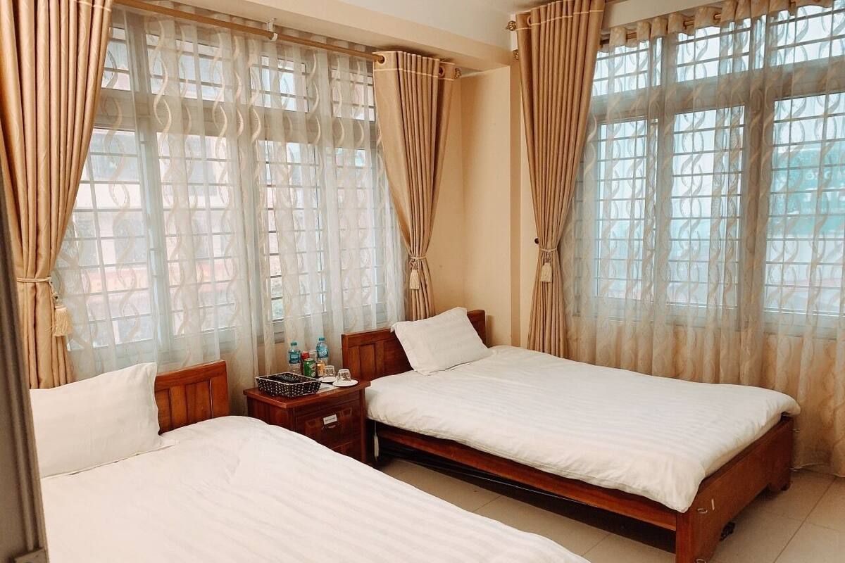 A hotel room with two beds, a wooden nightstand, and a window with patterned curtains.