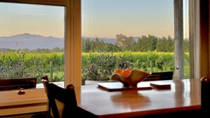 Ein Essbereich mit Tisch, Stühlen und Blick auf einen Weinberg durch große Fenster.
