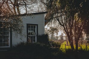 Een wit huis met een raam en een deur, omringd door bomen en een hek.