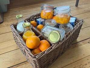 Een rieten mand gevuld met sinaasappels, een fles sap en verschillende glazen potten.