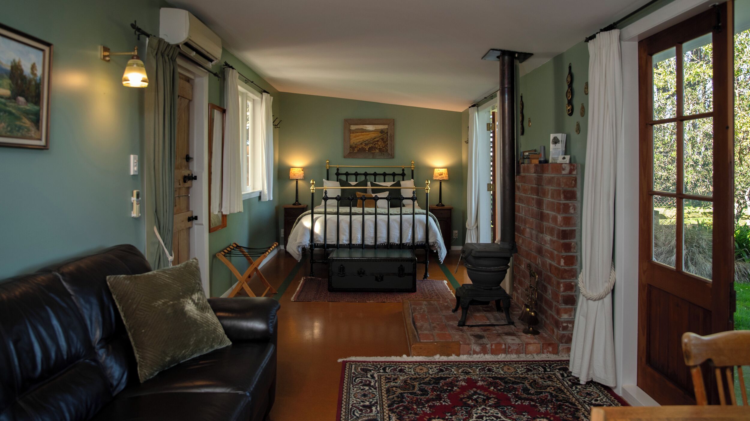 Un dormitorio acogedor con una cama, un banco de madera, un sofá de cuero negro y un tapete estampado.