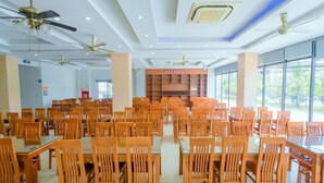 A spacious dining area with multiple wooden tables and chairs, ceiling fans, and a large window providing a view of the outdoors. - UFJ Hotel SS - by Bay Luxury (Sam Son)