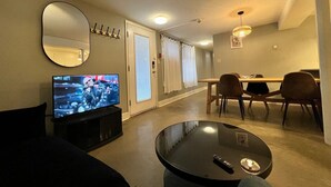 En stue med fjernsyn, et rundt sofabord og et spiseområde med stole og bord.
