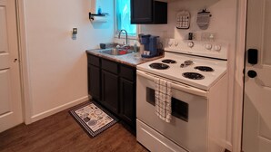 A kitchen with a white stove, black cabinets, a window with blue curtains, and a wooden floor. - Charming 1-bd house in Downtown Farmington, 1block from Police & Fire stations (Farmington)