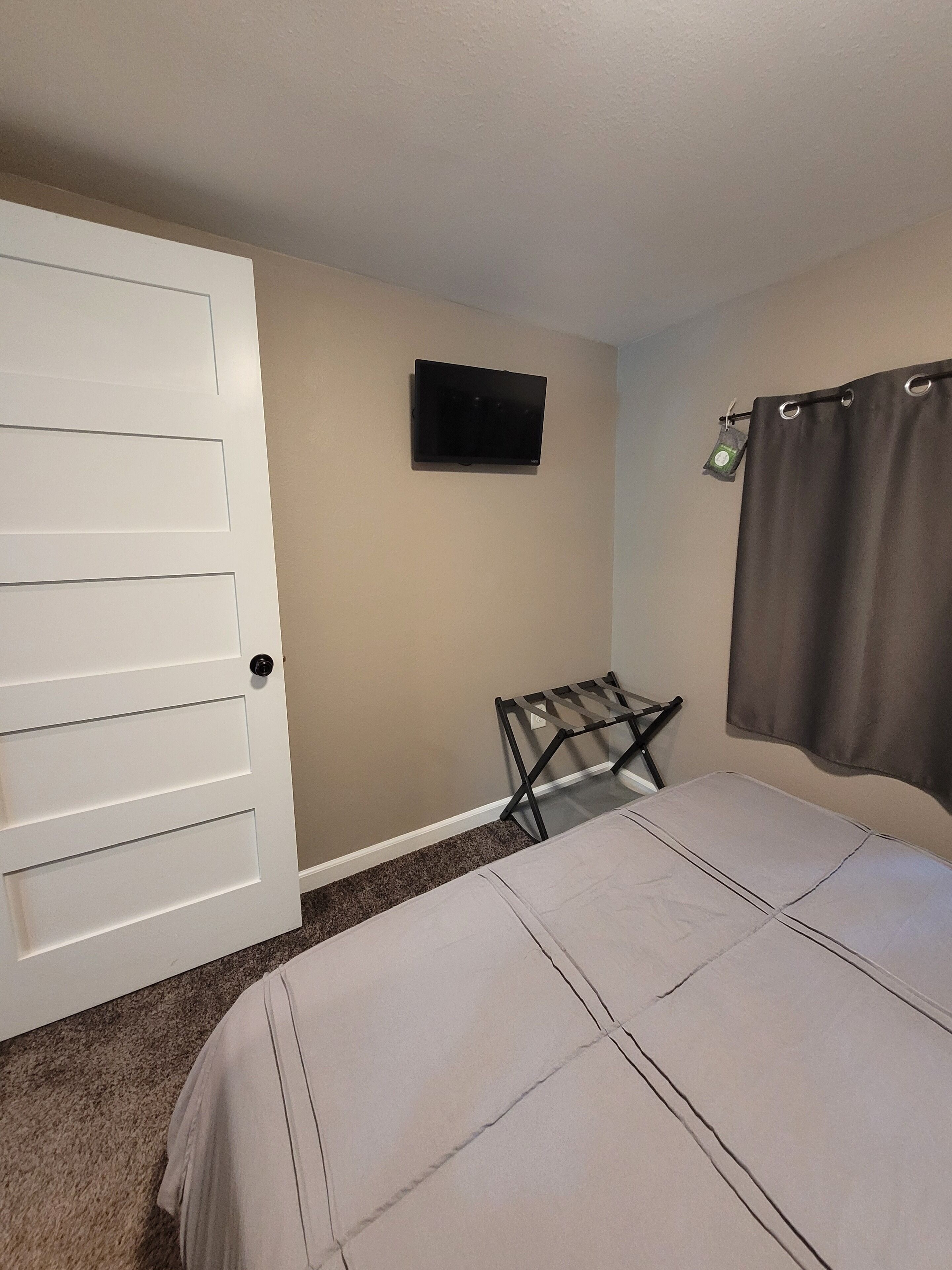 Una camera da letto con un letto, una TV a muro, una porta e una tenda.