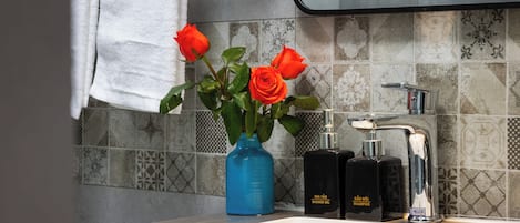 A bathroom with a sink, a mirror, a towel hanging on the wall, and a vase with roses.