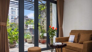 A modern living room with a sofa, a small table, and a view of a balcony with potted plants and a cityscape. - Hanoi Old Quarter Hotel and Spa (Hanoi)
