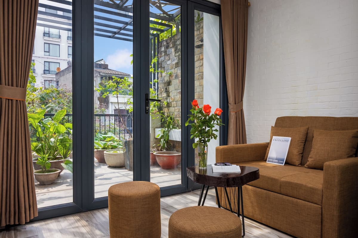 Una sala de estar moderna con un sofá, una mesita y vistas a un balcón con plantas en macetas y un paisaje urbano.