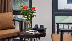 A room with a brown sofa, a small table with a vase of red roses, a pair of glasses, and a book. - Hanoi Old Quarter Hotel and Spa (Hanoi)