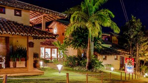 A well-lit building with a tiled roof, surrounded by lush greenery and palm trees. - Baixu Village (Porto Seguro)