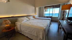 A hotel room with two beds, a desk, a lamp, and a view of the ocean. - Baixu Village (Porto Seguro)