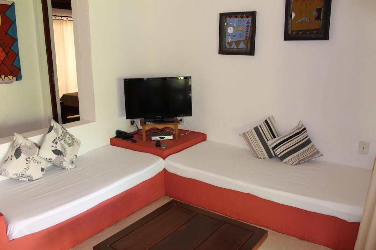 A room with two beds, a television on a wooden stand, and artwork on the walls.