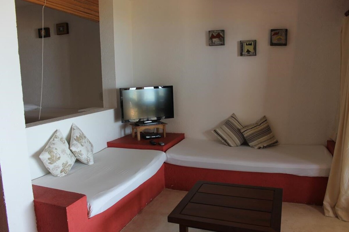 A room with a sofa, a television on a stand, a small table, and a wall with pictures.
