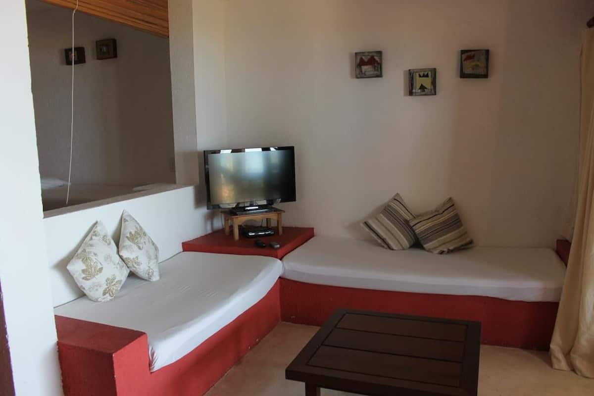 A room with a sofa, a television on a stand, a small table, and a wall with pictures.