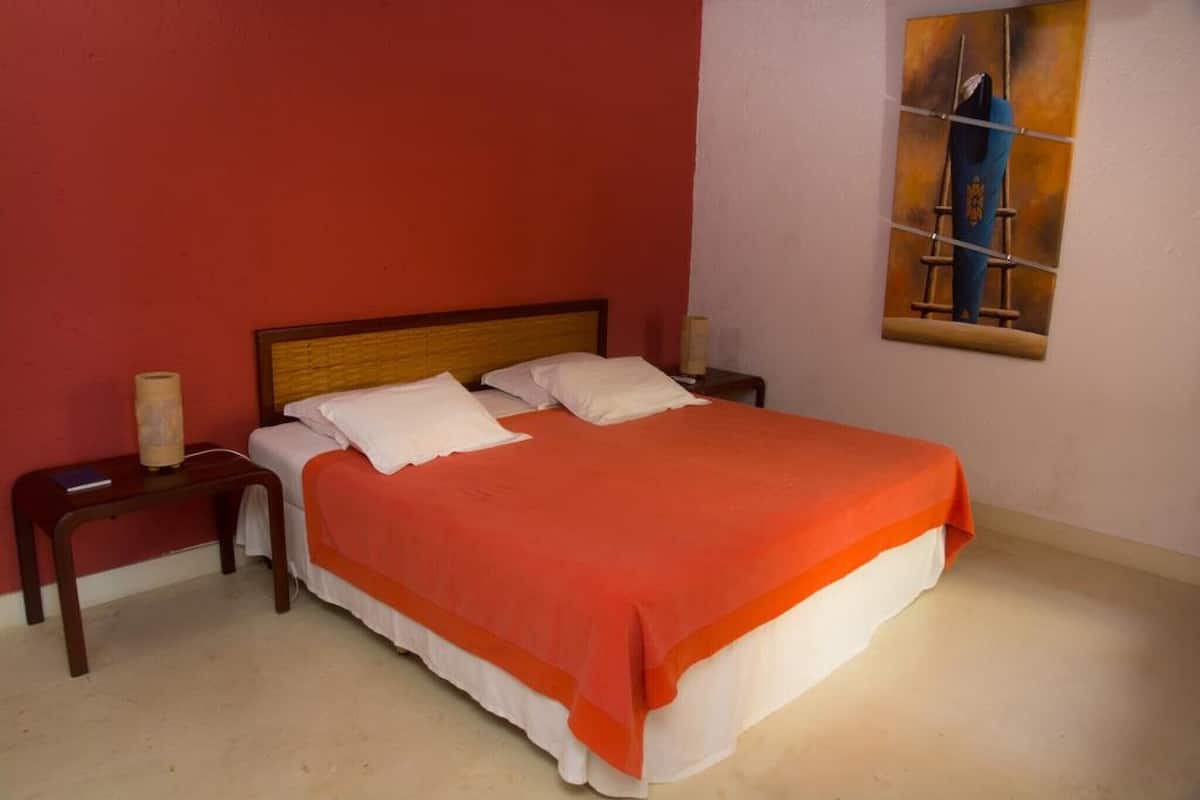 A bedroom with a bed, two bedside tables, a nightstand, and a painting on the wall.