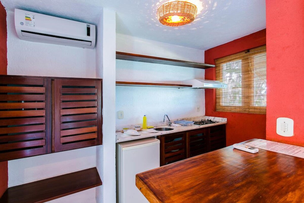 A compact kitchen with a built-in stove, a sink, and a window with blinds.