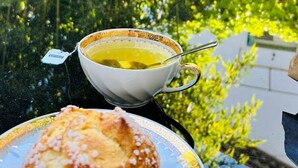 A table with a cup of tea and a pastry, surrounded by greenery.