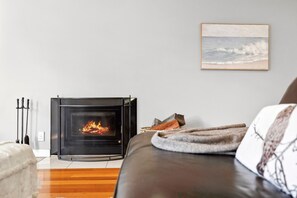 A cozy living room with a fireplace, a framed artwork on the wall, and a comfortable sofa. - Surphy G (Anglesea)