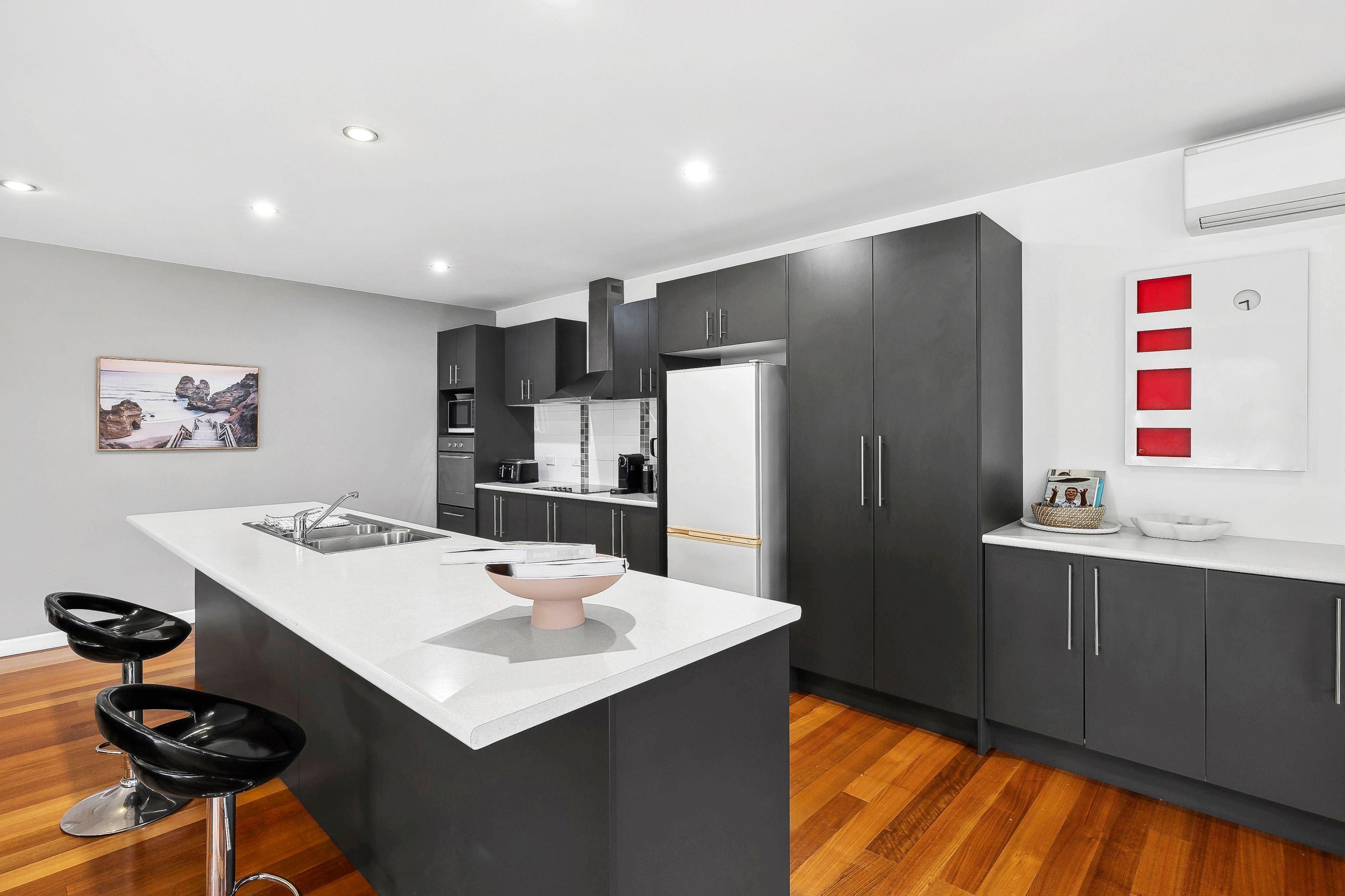 A modern kitchen with a central island, dark cabinetry, and a white countertop.