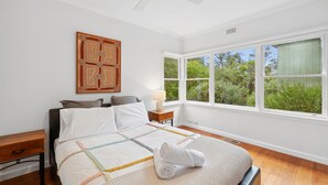 A bedroom with a bed, a nightstand, a window with a view of greenery, and a ceiling fan. - Surphy G (Anglesea)